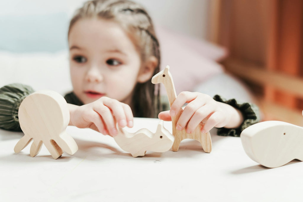 Kind spielt mit minimalistischen Holz-Tierfiguren auf hellen Hintergrund – natürlich, pädagogisch & emotional ansprechend