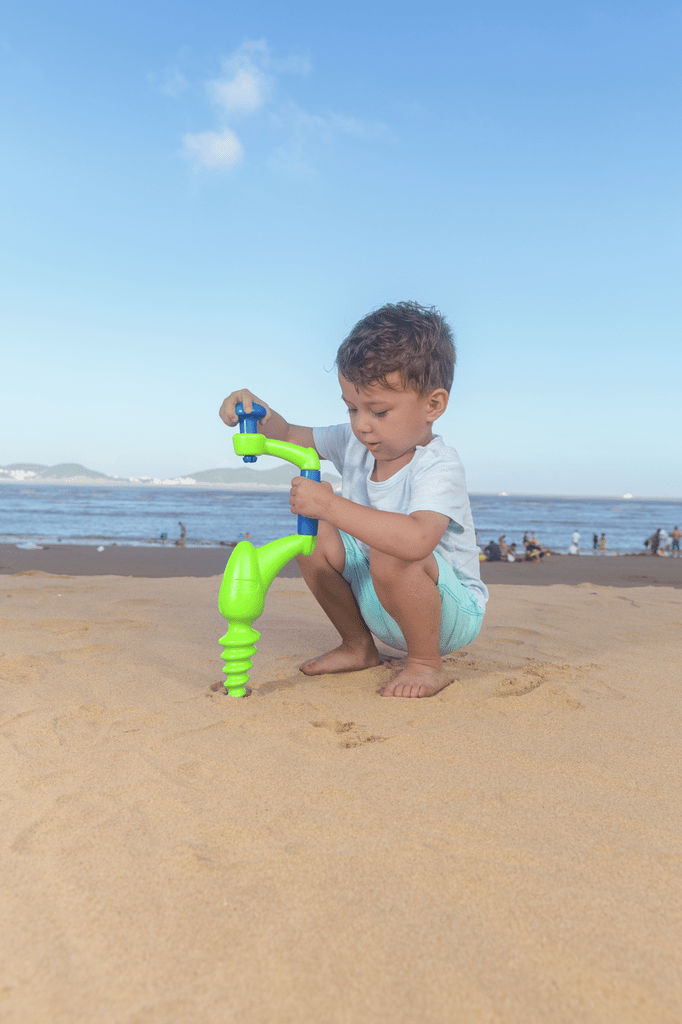 Kind spielt mit Hape Sandbohrer im feuchten Sand