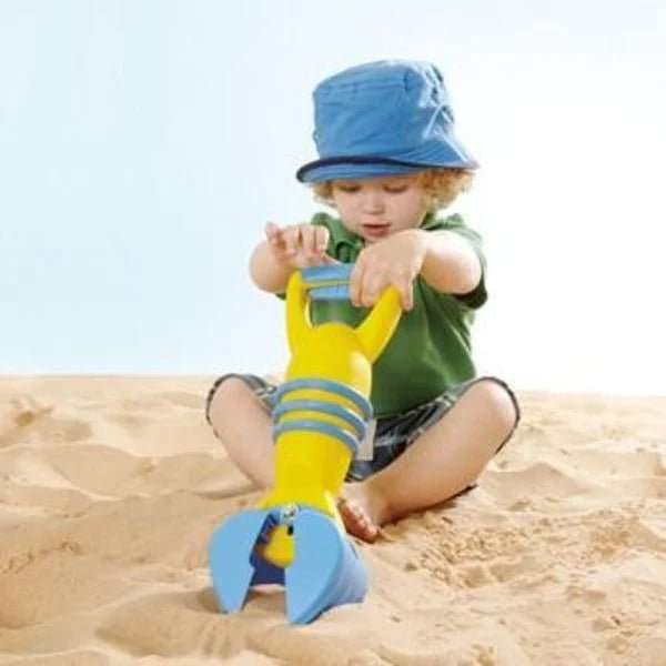 Kind benutzt gelben Greifarm zum Aufnehmen von Sand